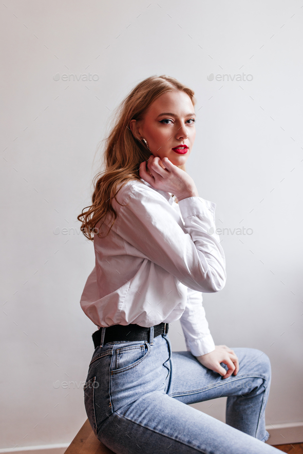 Sensual woman in jeans looking at camera. Studio shot of magnificent blonde  girl in white shirt. Stock Photo by look_studio