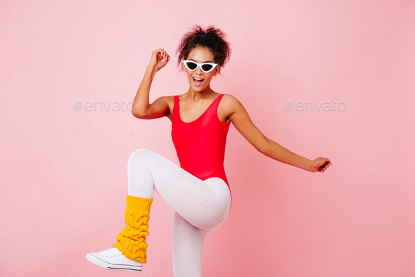 Excited shapely woman doing exercises on pink background. Stylish african  girl in red bodysuit enjo Stock Photo by look_studio