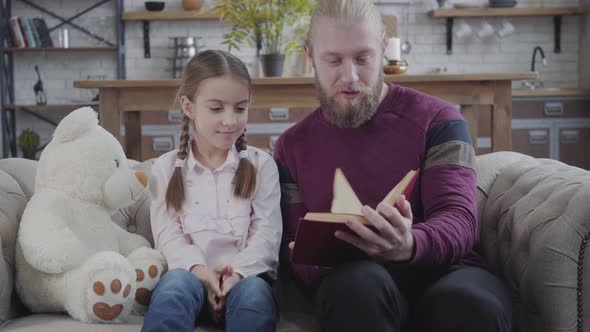 Positive Caucasian Father Turning Page and Touching Daughter's Nose. Cute Teenage Girl Smiling  alt