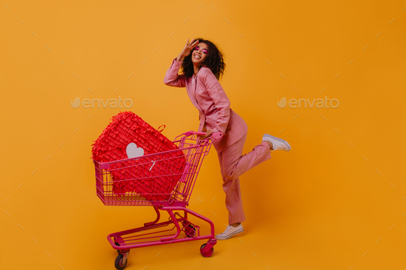 Blithesome black woman with wavy hair dancing during shopping. Indoor photo of excited african lady