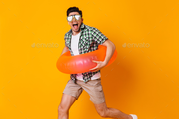 Guy in diving mask and inflatable circle runs on orange background