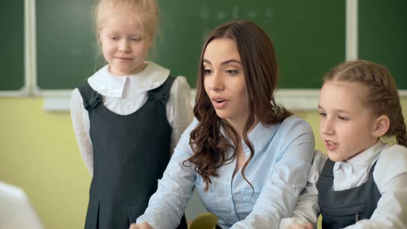 Happy Teacher Using Laptop with Pupils in the Classroom alt