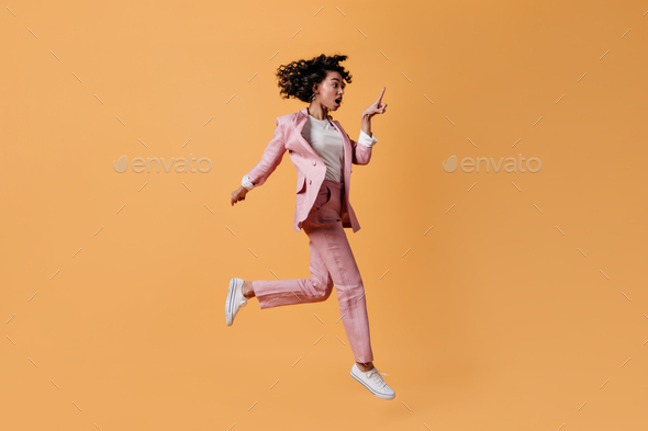 Shocked female model jumping on yellow background. Full length view of emotional mixed race woman i