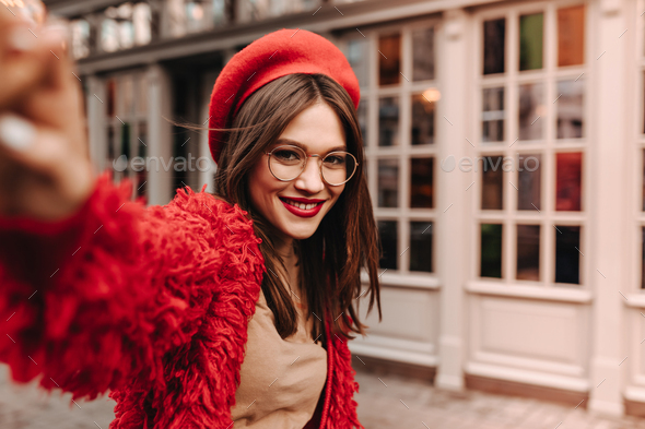 Adorable tanned lady in glasses dressed in red wool jacket, beige