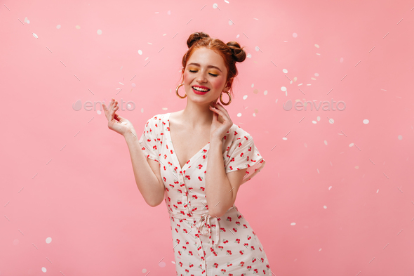 Charming lady in white dress with cherries smiles affably. Portrait of redhead girl in massive earr