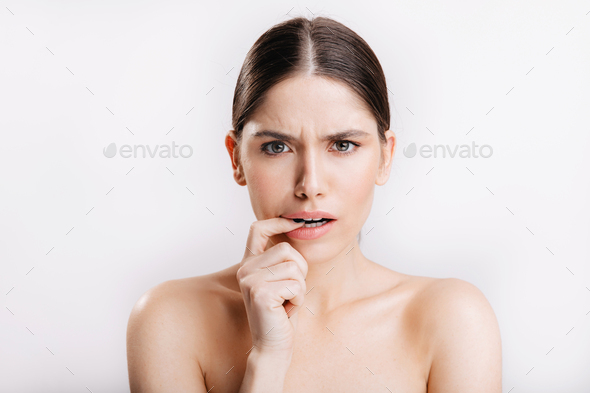 Model without makeup posing on white background. Portrait of displeased woman biting from doubt fin