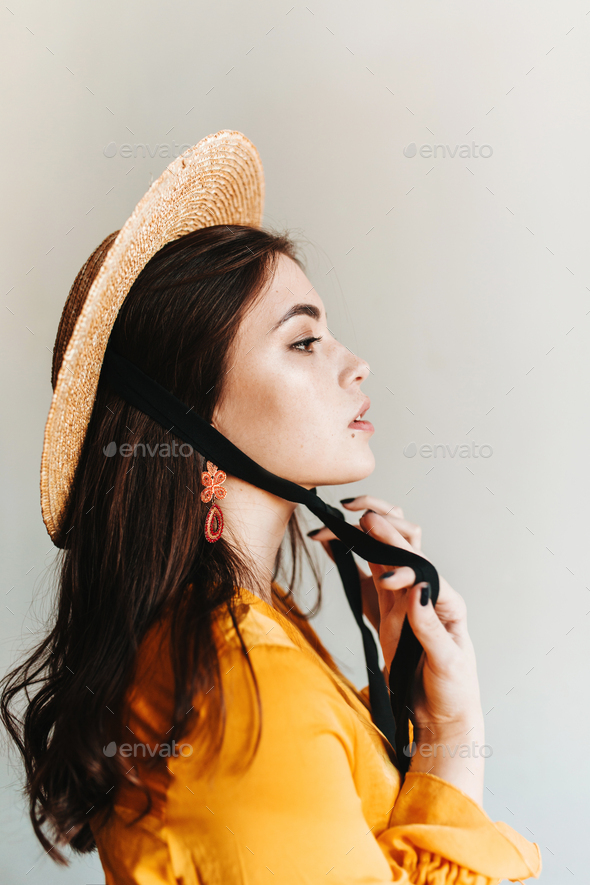 Profile shot of proud European girl with long hair in orange hat. Aristocrat woman in boater posing