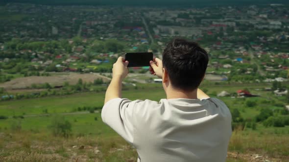 A Young Adult Male Takes a Smartphone Picture From the Top of a Large Hill alt
