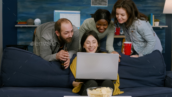 Group of mixed race people chilling on couch looking at laptop computer