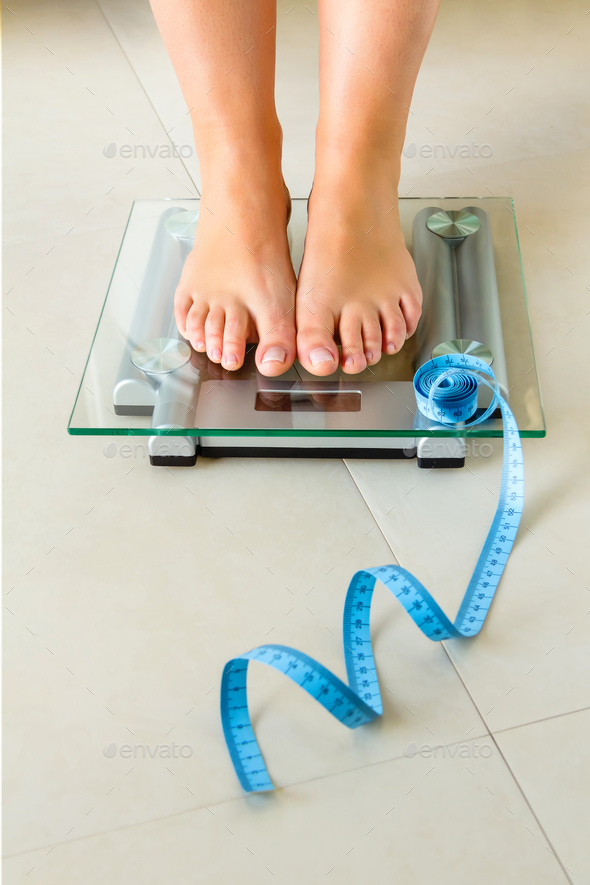 Woman feet standing on bathroom scale and tape measure