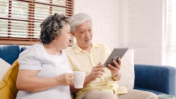 Asian elderly couple using tablet and drinking coffee in living room at home. - Stock Photo - Images