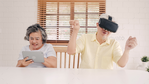 Asian elderly couple using tablet and virtual reality simulator playing games in living room.