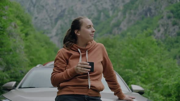 Woman traveler drinking hot tea  and looking at mounain view during a car summer trip alt
