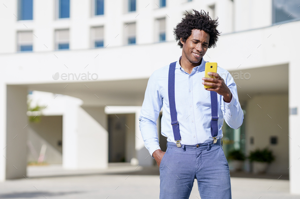 Black man with afro hairstyle using a smartphone near an office building  Stock Photo by javi_indy