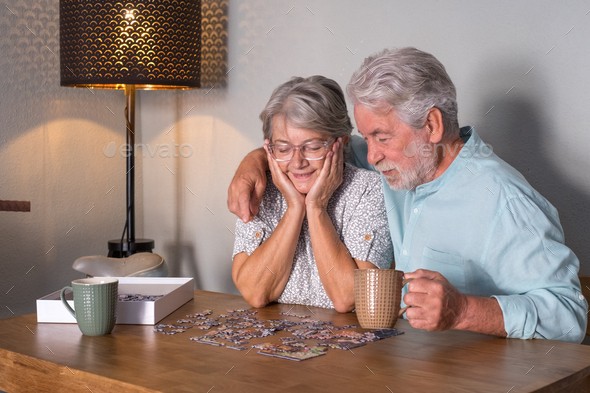 Happy Senior Couple At Home Spend Time Together Doing A Puzzle On The Wooden Table Stock Photo By Lucigerma