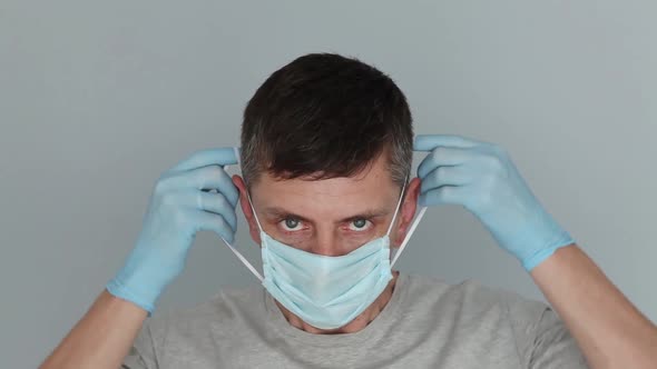Young man in rubber blue gloves puts on medical mask and  looking at camera