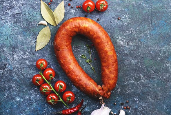 Smoked sausage circle on blue kitchen table with spices, tomatoes and garlic - Stock Photo - Images
