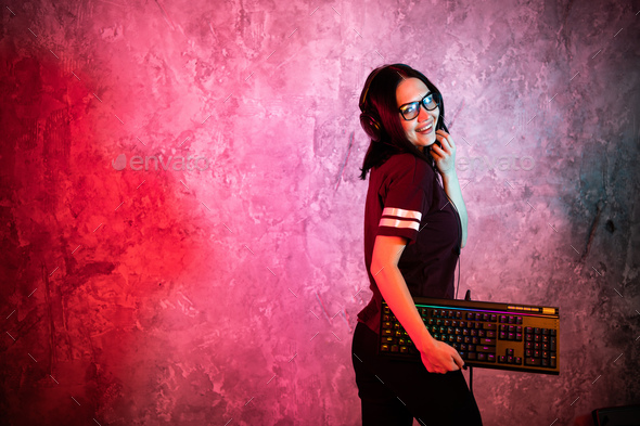 Female esports gamer posing with a gaming gear in neon light. Streamer girl standing with a gaming