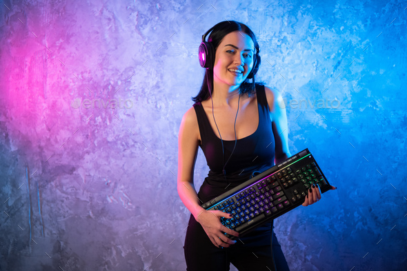 Portrait of the Beautiful Young Pro Gamer Girl standing with a gaming keyboard and headset and Looks - Stock Photo - Images