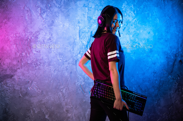 Female esports gamer posing with a gaming gear in neon light. Streamer girl standing with a gaming