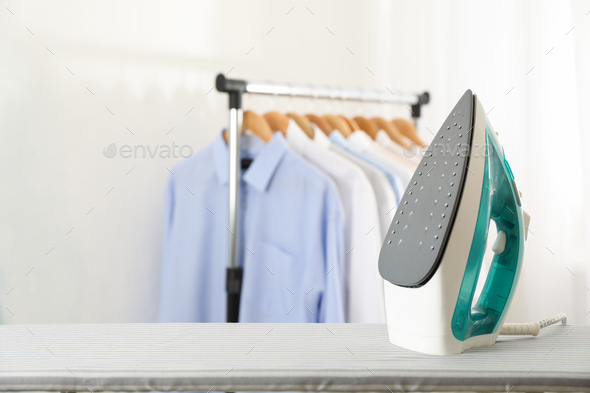 Iron on ironing board against light background, space for text Stock Photo  by AtlasComposer