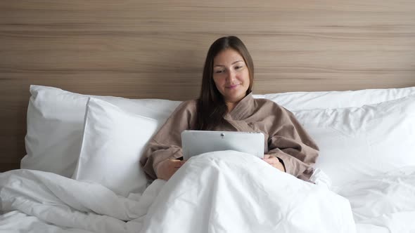 Girl in Bathrobe Studies Online with Tablet in Hotel Bed alt