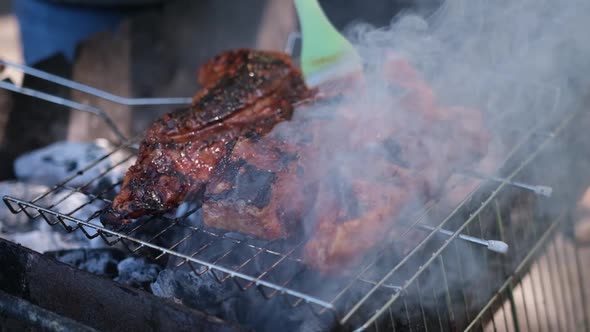 Delicious Beef or Pork Ribs Frying on a Charcoal Grill Being Covered with Red Gravy Sauce Brush alt