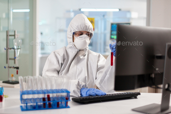 Medical researcher dressed in ppe suit looking at blood sample