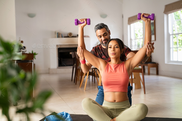 Personal trainer helping woman to do exercise at home Stock Photo by Rido81