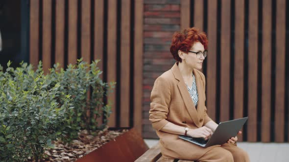 Redhead Businesswoman Working on Laptop on Street alt