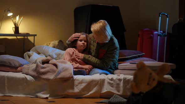 Wide Shot Loving Ukrainian Mother Talking with Scared Daughter Sitting in Bomb Shelter alt