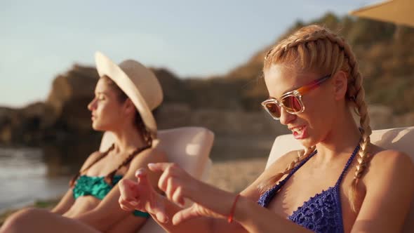 Two Young Beautiful Girls Laughing at the Sea Side Sitting in Chaise Lounges alt