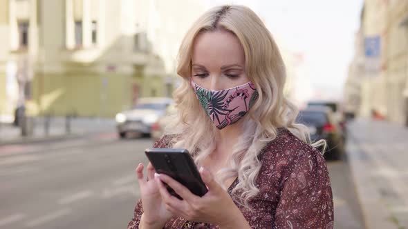 A Middleaged Caucasian Woman in a Face Mask Works on a Smartphone in an Urban Area alt