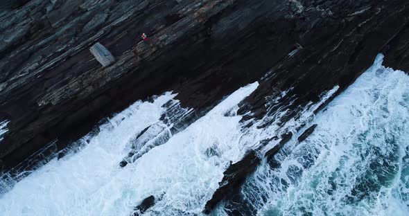A man watching the waves hit the rocky cliff down below in Curtis island lighthouse Camden Maine USA alt