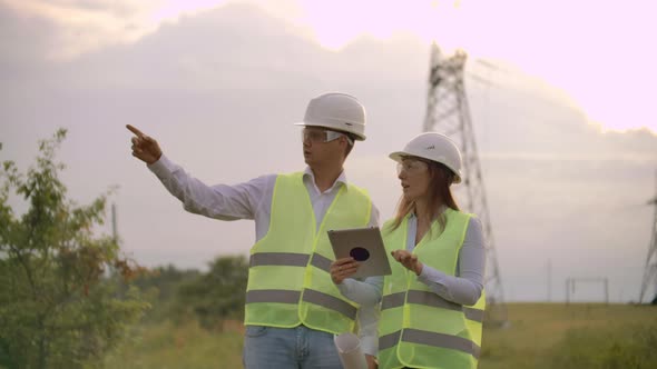 Engineers in Uniform Working with a Laptop Near Transmission Lines alt