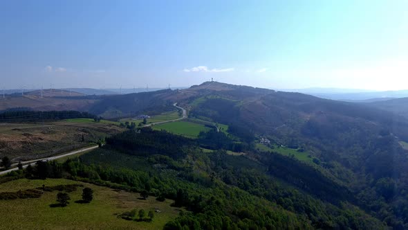 Small ecological farms in the mountains with forests and meadows connected by a road and wind turbin alt