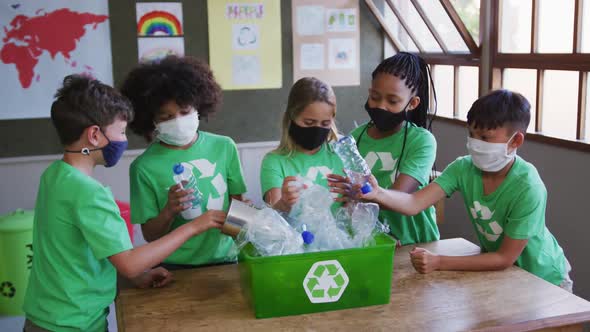 Group of kids wearing face masks putting plastic items in recycle container alt
