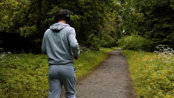 Fit Man Athlete Running at Park with Big Black Headphones alt