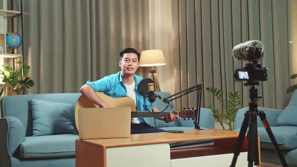 Asian Man Is A Vlogger With Guitar Looking To Camera. Live Streaming alt