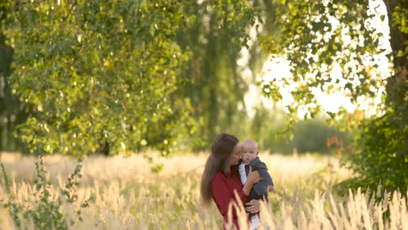 Happy young mum and baby walking together outdoor enjoy beautiful field of sunshine alt