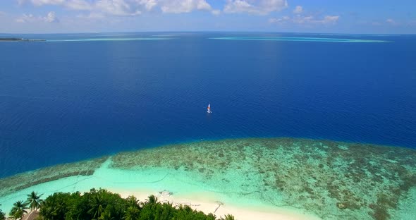 Aerial drone view of a man and woman sailing on a boat to a tropical island alt