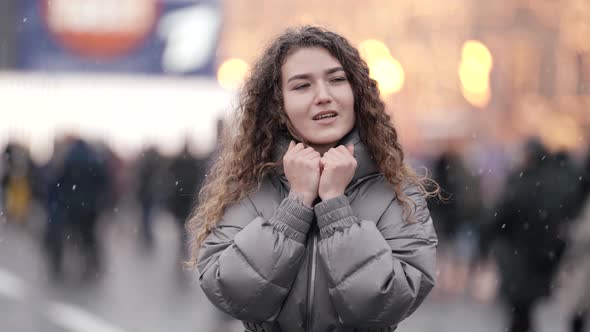 Portrait of a Young Woman with Curly Hair Standing on a Crowded City Street on a Cold Day alt