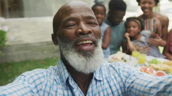 Portrait of happy african american family taking selfie and having breakfast in garden alt