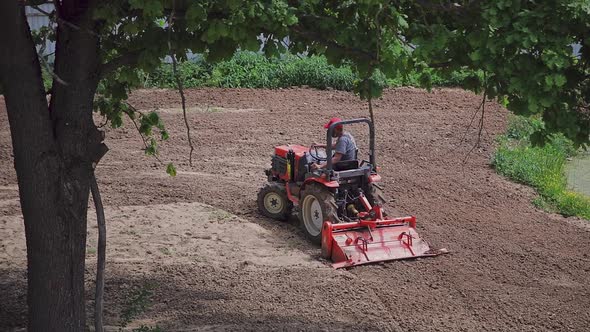 A peasant on a mini-tractor plows the land, loosens the land. View from above.