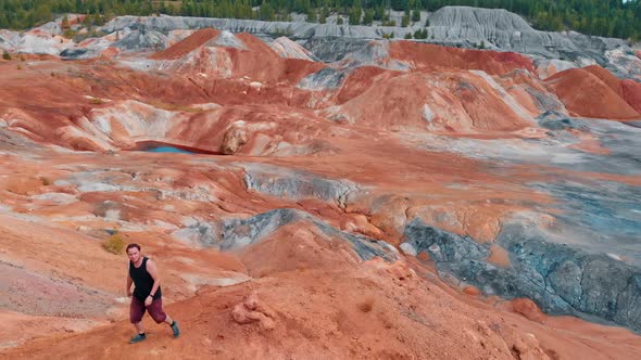 A Man Walking on the Top of an Orange Clay Mountain - Red Ponds Around alt