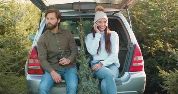 Woman which Sitting Together with Her Husband in Car's trunk Among Beautiful Fir Trees alt
