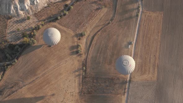 White Hot Air Balloons Fly Over Wide Brown Fields and Road alt