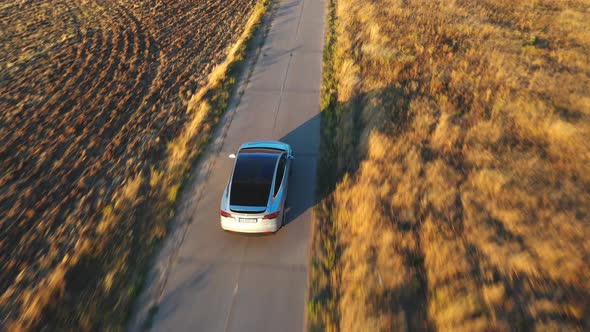 Aerial Shot of Electrical Car Driving on Country Road at Sunny Day alt