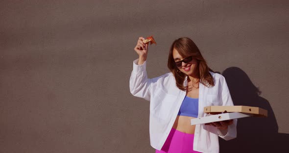 beautiful girl dancing with pizza in her hands near the wall