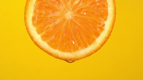 Natural oil drop falling from orange on yellow background. Orange slice and water splashing, drops alt